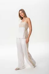 Pantalón sastrero de lino color blanco crudo, de corte ancho y tiro alto, con una guarda de broderie color crudo a lo largo de la costura lateral exterior de cada pierna.