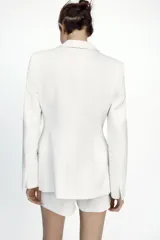 Blazer entallada color blanco, con cuello solapa combinado, manga larga con hombreras, bolsillos de plastrón en delantero, detalle de costuras marcadas, forro interior a tono y cierre frontal con botón forrado en mismo material.