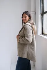 Tapado de paño con capucha, color beige, con cierre frontal, bolsillos laterales y puños vueltos en tono más claro.