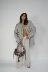 Bolso marrón con efecto desgastado y detalles pintados en blanco. Tiene forma de media luna, correa de hombro y cierre con hebilla plateada.