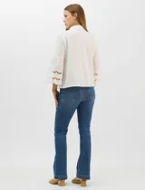 Camisa negra de poliéster con cuello camisero, escote en V y cierre frontal de botones. Cuenta con mangas anchas de corte acampanado y detalles de bordado suizo calado en las mangas y en el ruedo inferior.
