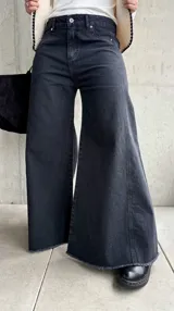 Jean de corte oxford y tiro medio, color negro lavado. Presenta diseño de pierna ancha con costuras verticales decorativas y ruedo deshilachado.