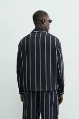 Sobrecamisa de hombre, corte relajado, color azul marino con rayas verticales blancas. Presenta cuello solapa, manga larga con puños abotonados, bolsillos de parche delanteros y cierre frontal de botones.