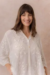 Camisa blanca de calce relajado con tejido semitransparente y bordados florales en relieve. Cuenta con cuello camisero, abotonadura frontal y mangas amplias.