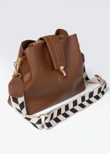 Cartera marrón de cuero sintético con tres compartimentos, cierre y correa con estampado geométrico en blanco y negro.