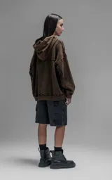 Hoodie de corte oversize y largo crop, confeccionado en algodón con efecto de desgaste y color óxido. Presenta costuras expuestas, detalles de roturas en los bordes y bolsillo frontal tipo canguro.
