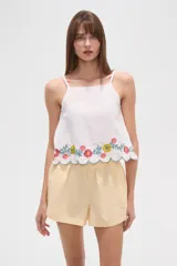 Top de algodón blanco con breteles finos regulables y escote cuadrado. Presenta un diseño holgado con bordado floral multicolor en el ruedo y terminación festoneada.