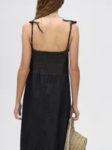 Vestido midi de denim color marrón, con corte holgado, breteles finos con lazos ajustables y detalle de volado en el ruedo.