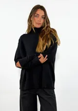 Sweater de punto negro con cuello alto, manga larga y diseño holgado. Presenta puños y ruedo acanalados.