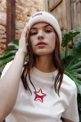 Gorro beanie tejido de punto grueso en color beige, con vuelta y pequeña etiqueta decorativa negra con la inscripción 'FEEL GOOD'.
