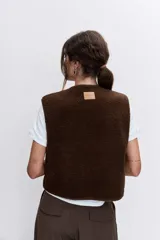 Chaleco de textura tipo corderito en color marrón chocolate, con cuello redondo, cierre frontal con botones y bolsillos laterales.