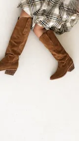 Bota estilo tejana de caña alta, confeccionada en gamuza color marrón, con taco cuadrado de madera y punta almendrada.