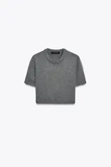 Jersey de punto gris oscuro, cuello redondo y manga larga. Presenta detalles desmontables con botones a lo largo de las costuras de las mangas y en el ruedo inferior.