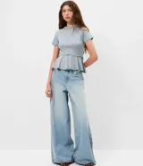 Blusa de punto Roma color celeste, con cuello alto, mangas cortas y diseño peplum. Presenta recortes estructurales y un cinturón integrado con hebilla metálica en la cintura, finalizando en un ruedo con volados.