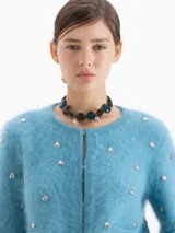 Cardigan de tejido de punto suave en color azul, con cuello redondo, cierre frontal y manga larga. Presenta pequeños apliques metálicos en forma de corazón distribuidos por toda la prenda.