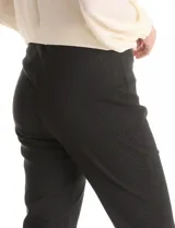 Pantalón de gabardina elastizada en color negro con finas líneas verticales de lurex que aportan un brillo sutil. Presenta un corte recto, cintura plana y aberturas frontales en el ruedo.