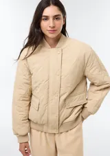Campera acolchada de color beige con diseño matelasseado, cuello, puños y dobladillo en rib elástico. Cuenta con bolsillos frontales con solapa y cierre de botones a presión.