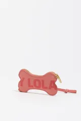Monedero pequeño de cuero reconstituido color rojo brillante, con forma de hueso de perro. Posee cierre de cremallera dorado y una correa corta de cuero para sujetar.