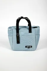 Lunchera rosa con asas negras y cierre superior. Tiene un bolsillo lateral y un logo con la inscripción "LUNCH BAG".