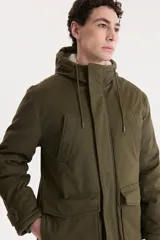 Campera parka larga color verde militar con capucha forrada en piel sintética. Tiene cierre frontal con cremallera y botones a presión, cuatro bolsillos delanteros con solapa y puños ajustables con botones.