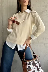 Sweater beige de hilo con cuello camisero blanco y botones decorativos en los hombros.