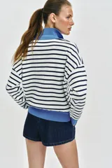 Sweater de punto con diseño a rayas horizontales en blanco y negro, manga larga, cuello polo en color celeste y cierre frontal parcial con cremallera.