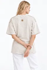 Remera oversize de algodón con acabado stonewash, color gris azulado, manga corta y cuello redondo. Cuenta con apliques bordados a mano en forma de hojas con canutillos plateados sobre los hombros.