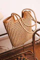 Bolso tipo tote bag de cuero trenzado a mano, en tonos marrón y negro, con asas trenzadas.