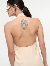 Mono color beige con escote halter, corte holgado, cinturón dorado y pantalones palazzo.