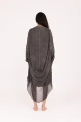 Camisa larga de fit amplio, color gris oscuro con efecto desgastado/lavado, cuello mao y cierre frontal de botones. Presenta mangas largas y un bajo asimétrico con terminación deshilachada.