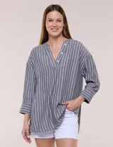 Blusa de silueta holgada a rayas verdes y blancas, confeccionada en tela liviana con textura arrugada. Presenta cuello en V profundo con botones frontales, mangas 3/4 de hombro caído y ruedo asimétrico con aberturas laterales.