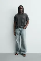 Camiseta de corte relajado con cuello redondo y mangas cortas. Presenta un efecto lavado que le otorga una apariencia única y estampados a contraste en el frente.