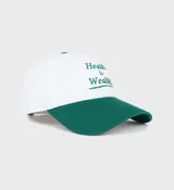 Gorro de béisbol blanco con visera verde y logo bordado en verde con la frase "Health is Wealth!".