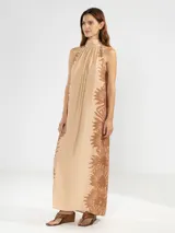 Vestido largo tipo maxi con cuello halter, sin mangas y corte holgado. Presenta un diseño estampado de flores en tonos marrones sobre una base de color beige.