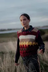 Chaleco tejido de punto con diseño de rayas horizontales y bloques de color en tonos bordó, beige, blanco y amarillo. Presenta cuello redondo y terminaciones acanaladas.