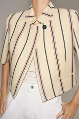 Blazer cropped ZW Collection confeccionada en mezcla de algodón, con diseño a rayas verticales en tonos azul y rojo sobre base beige. Presenta cuello redondo, manga corta, forro interior a tono y cierre frontal con un botón.