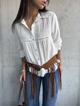 Camisa blanca de corte clásico con cuello camisero, mangas largas y detalle de bordado geométrico en el panel frontal superior. Confeccionada en tela liviana con textura.