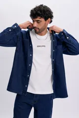 Sobrecamisa de jean color azul oscuro, de corte oversize, con mangas largas, bolsillos frontales con solapa y cierre con broches a presión.