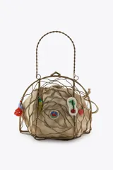 Bolso rígido con estructura metálica dorada y forro interior de tela color beige ajustable con lazada. Decorado con charms colgantes de diferentes motivos y asa superior rígida.