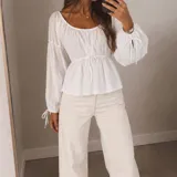 Blusa blanca de manga larga abullonada con tiras para ajustar en los puños, escote bote y cordón ajustable en la cintura.