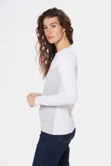 Buzo de tejido de punto con diseño bicolor, combinando blanco en la parte superior y mangas con un tono celeste grisáceo en el cuerpo, presentando un patrón geométrico en la unión de los colores. Posee cuello redondo y mangas largas.