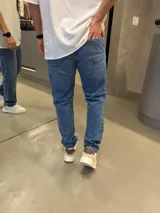 Jean de corte mom con calce regular, confeccionado en denim de tono azul medio. Presenta diseño clásico de cinco bolsillos y cierre frontal.
