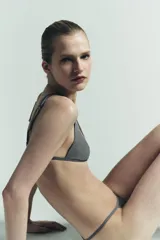 Tanga de tiro medio color gris oscuro, con cintura elástica y paneles laterales de tul semitransparente en tono rosado pálido.