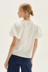 Blusa blanca de calce recto con cuerpo de jersey y mangas cortas tipo globo en popelina. Presenta cuello redondo y detalle de bordado decorativo en la espalda.