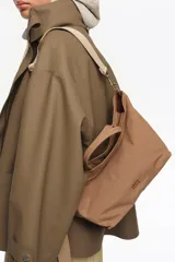 Bolso shopper mediano de mano Bimba y Lola color marrón, confeccionado en poliamida con detalles en cuero y herrajes metálicos dorados. Cuenta con doble asa de mano, correa de hombro ajustable de lona beige, cierre superior con cremallera y logo impreso en dorado al frente.
