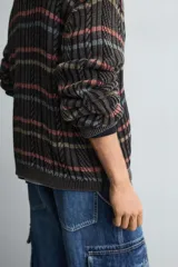 Jersey de punto con ajuste relajado, cuello redondo y manga larga. Presenta un diseño de rayas horizontales multicolores sobre una base oscura con textura de ochos y efecto lavado.