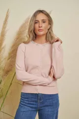 Saco de punto color rosado, con cuello redondo y cierre frontal abotonado. Presenta detalles de strass alrededor del cuello y en los botones.