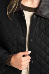 Campera negra de diseño capitoneado con cuello de solapa en contraste color marrón. Presenta cierre frontal con cremallera y botones a presión, mangas largas con puños ajustables y un corte recto.