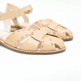 Sandalias planas de cuero color vainilla con tiras cruzadas, tachas metalizadas decorativas y tira con hebilla ajustable al tobillo.