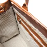 Cartera tipo tote de cuero texturizado color suela, con doble asa de mano y correa larga ajustable y extraíble. Presenta el logo de la marca grabado en el centro y cierre superior.